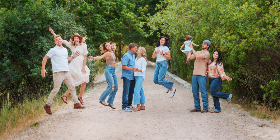 Vineyard family playfully leaping in place on a gravel road in front of a forest